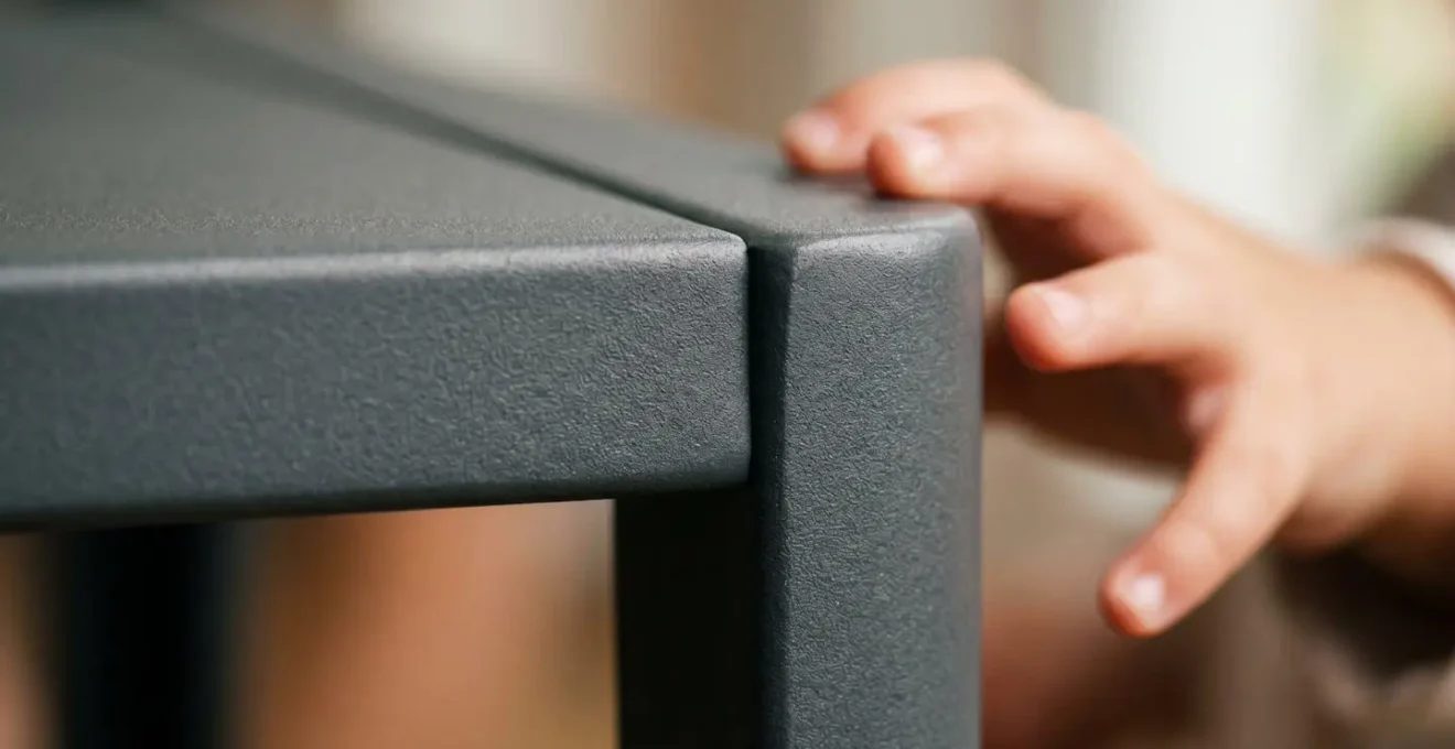 Macro close-up of powder-coated steel furniture edge showing smooth non-toxic finish safe for children with shallow depth of field