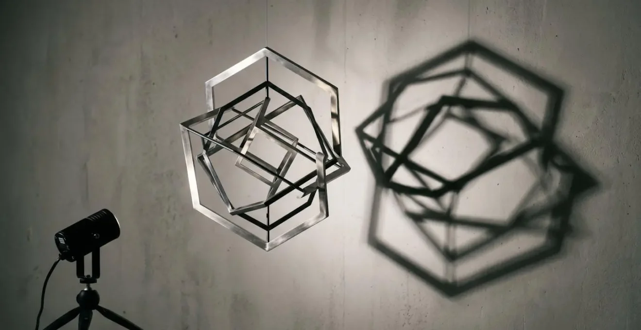Dramatic low-angle spotlight creating sharp elongated shadows from kinetic sculpture elements on textured wall