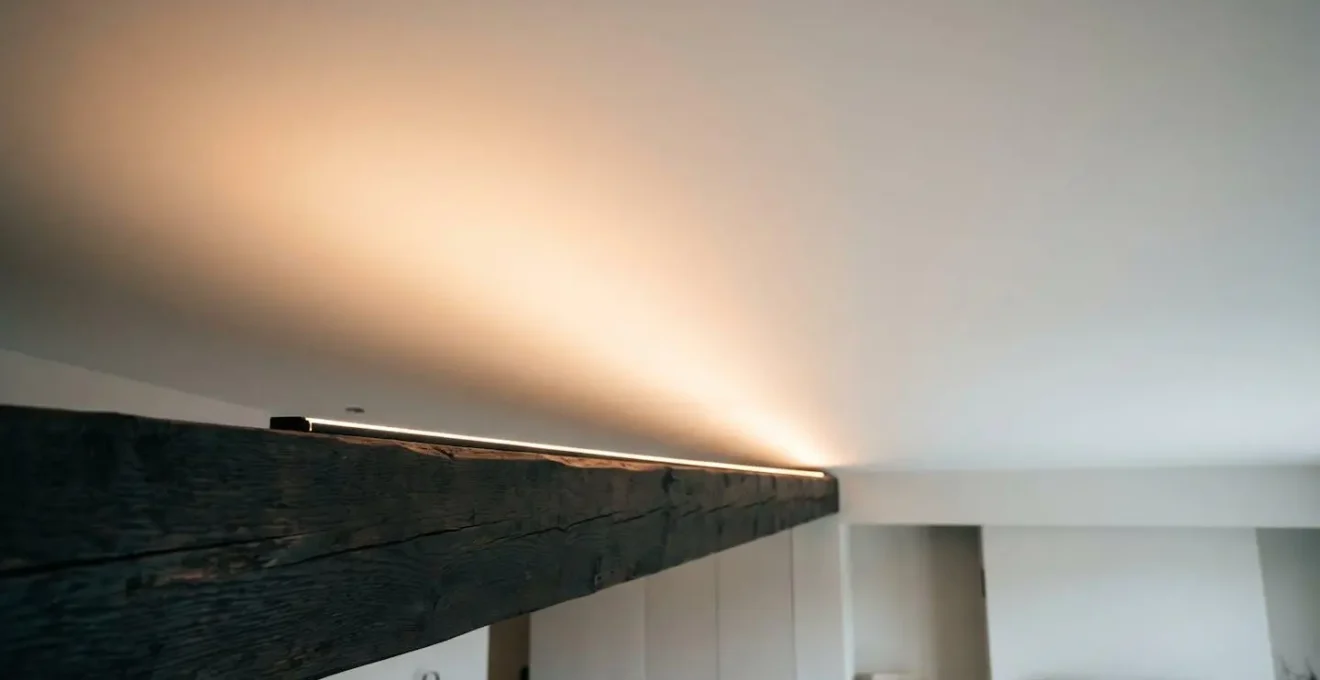 Low-angle architectural view showing LED strip installed atop exposed beam casting soft upward glow onto white ceiling surface